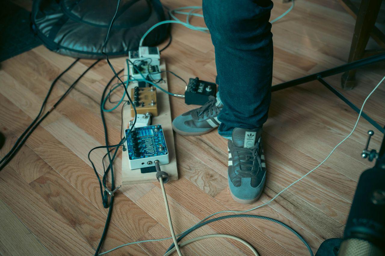 About Casual musician setting with foot on a set of guitar effects pedals on a wooden floor.