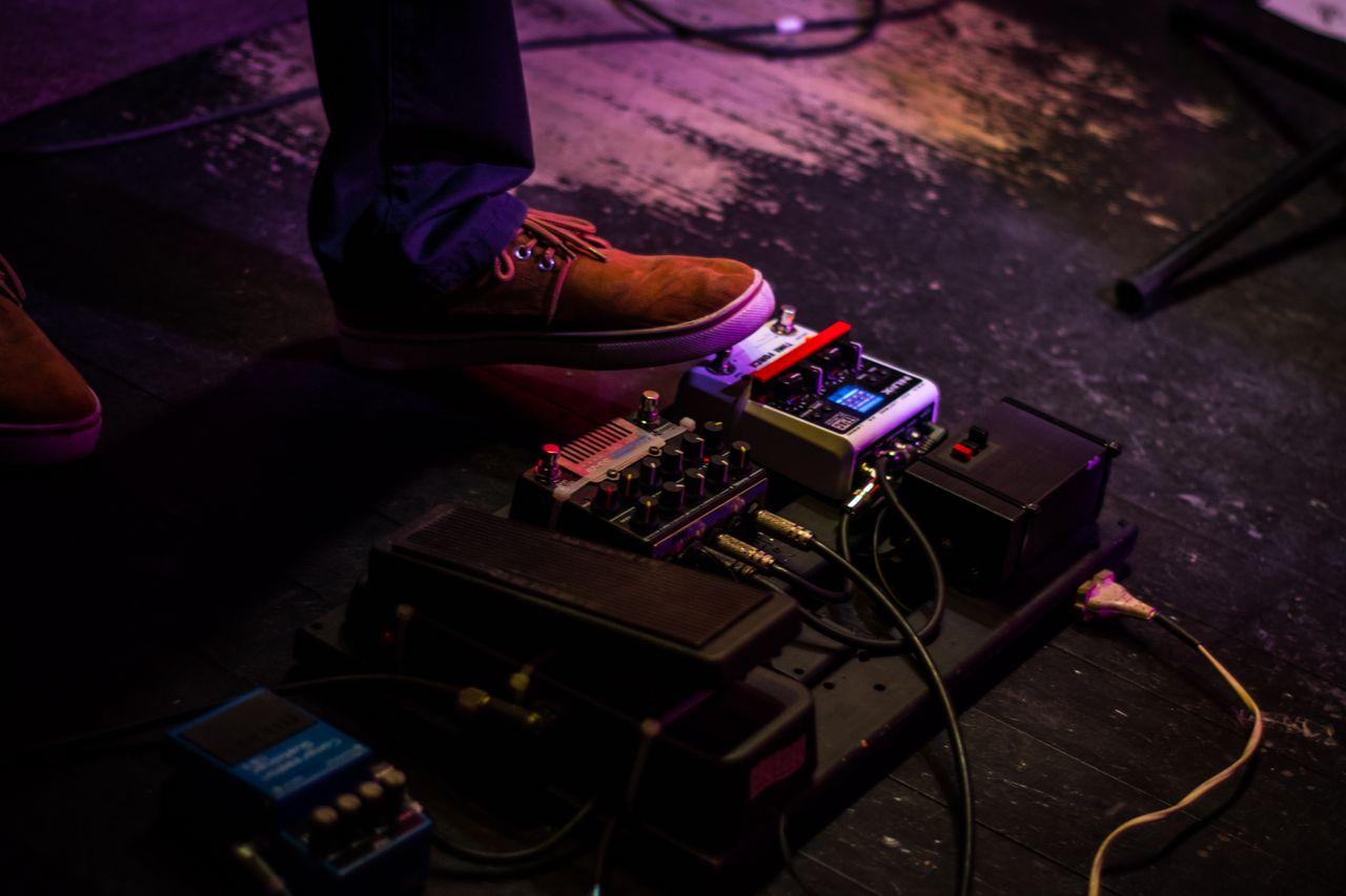 Home Close-up of a musician's foot operating a guitar pedal board during a live performance.